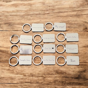 May include: A collection of 10 silver keychains with engraved messages. The messages include "My angel", "Buster Bishop x", "We love you Daddy", "Love You", "My world x", "Drive safe Grandad Sean love Amelia x", "Famiglia Sena", "Sue's New House Keys", and "Nan".