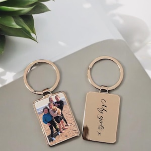 May include: Two gold metal keyrings with a photo of four girls and a dog on one keyring and the text "My girls" on the other keyring.