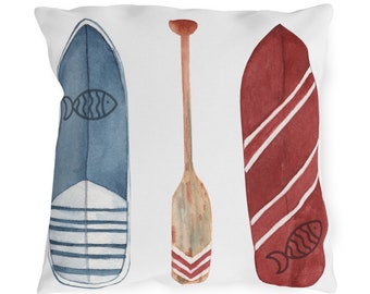 May include: White square pillow with a nautical design. The pillow features watercolor illustrations of a blue boat, a wooden oar, and a red boat. The blue boat has a fish illustration and white stripes. The red boat has white stripes and a fish illustration.