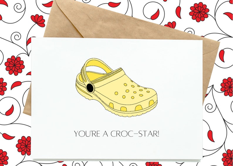 K&ouml;nnte beinhalten: Eine gelbe Karte mit einer Cartoon-Zeichnung eines gelben Clogs mit schwarzen Akzenten. Die Karte sagt "You're a croc-star!"
