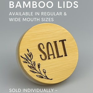 Może przedstawiać: Okrągła drewniana pokrywka z wygrawerowanym w środku napisem "SALT" (SÓL). Pokrywka ma naturalne usłojenie drewna i mały, wygrawerowany wzór kwiatowy z boku.