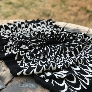 May include: Black and white patterned fabric with a swirling design. The fabric is folded and draped on a wooden surface.