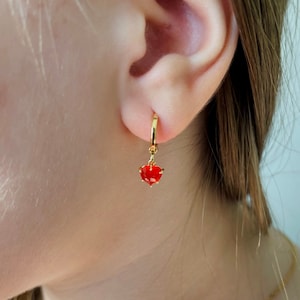 May include: Gold hoop earrings with a dangling red heart-shaped charm.