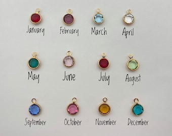 May include: Twelve circular gold-toned charms, each featuring a different colored gemstone representing a month of the year. The charms are arranged in three rows of four, with the corresponding month name printed in black text below each charm.