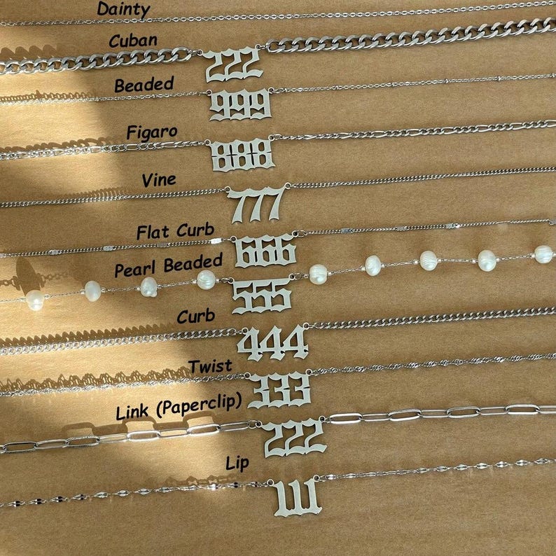 May include: A collection of ten silver-toned necklaces, each featuring a different chain style and a unique three-digit number pendant in an old English font. The styles include dainty, cuban, beaded, figaro, vine, flat curb, pearl, curb, twist, link, and lip.