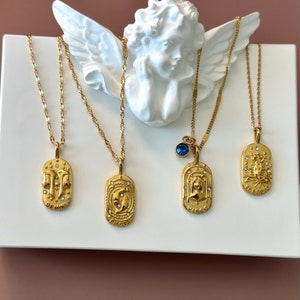 May include: Four gold-toned necklaces with oval pendants featuring zodiac signs Gemini, Pisces, Virgo, and Scorpio. Each pendant is embossed with a symbol, small clear crystals, and the name of the sign. One necklace includes a small blue crystal charm.