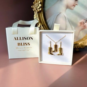 May include: A white gift box with gold lettering that reads "Allison Bliss" and the phrase "You are so beautiful in every single way!"  The box contains a gold necklace and earrings with a cowboy boot charm.