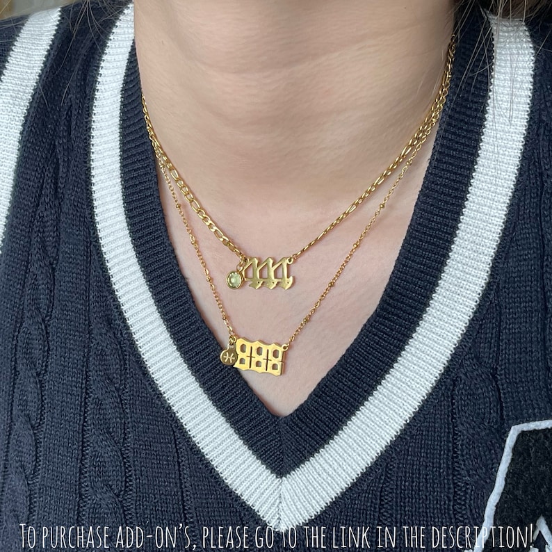 May include: Two gold-toned layered necklaces featuring gothic-style number pendants. The top necklace displays the number 444 with a small green circular charm, while the bottom necklace features the number 888 with a small circular Pisces symbol charm.