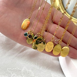 May include: A selection of gold-coloured necklaces, each with an oval pendant. The pendants display floral designs and hang from fine chains. Some necklaces have gemstone embellishments. The words "June Rose" are engraved on one pendant.