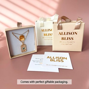 May include: A gold-toned layered necklace with a rectangular pendant featuring a green stone, housed in a beige gift box labeled ALLISON BLISS. Includes a white card with the text ALLISON BLISS and a thank you note with gold foil lettering.