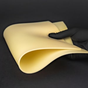 May include: A close-up of a light yellow practice skin for tattooing. The skin is flexible and has a smooth surface.