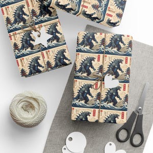 May include: Wrapping paper with a repeating pattern of a Godzilla-like monster in a Japanese wave design. The monster is depicted in a blue and black colour scheme, with a red and white background. The paper is wrapped around a gift box with a brown twine bow.
