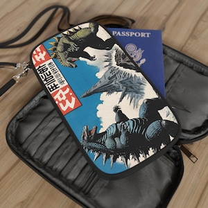 May include: A black travel wallet with a colorful illustration of a monster battling a jet plane. The wallet has a strap and zipper closure. A blue passport is visible inside the wallet.