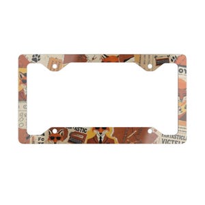 May include: A rectangular license plate frame featuring a collage pattern of orange foxes wearing suits and sunglasses, typewriters, and paw prints. The text "FANTASTIC" and "VICTEL" is visible on the cream and brown background of the frame.