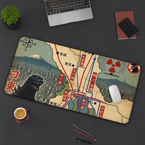 May include: A rectangular desk mat featuring a vintage-style map illustration of Tokyo with a large black monster figure, Mount Fuji, a radiation symbol, and various Japanese text characters. The design includes red and blue transit lines on a beige background.