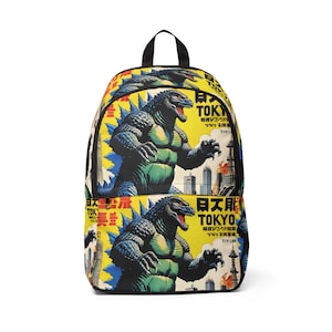 May include: A backpack featuring a Godzilla design with a yellow background and Japanese text. The design includes a large Godzilla illustration in shades of green, blue, and black. The backpack has a black handle and straps.