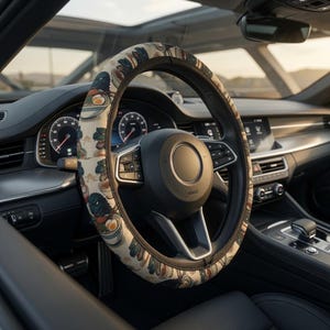 Peut inclure: Un couvre-volant avec un motif répétitif représentant une créature sombre mangeant un bol de ramen avec des œufs et des oignons verts sur un fond beige clair. La housse est installée sur un volant noir à l'intérieur d'un véhicule.