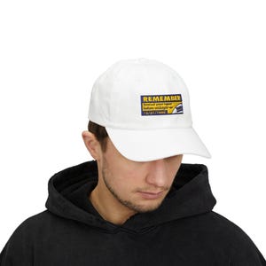 May include: White baseball cap with a rectangular patch that reads "REMEMBER" in yellow text on a blue background. Below the word "REMEMBER" is the text "Rewind your tapes before midnight on 12/31/1999" in white text on a blue background.