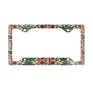 May include: License plate frame with a floral pattern. The frame features a cream background with a repeating design of red flowers, green leaves, and blue and yellow accents. The frame has a rectangular shape with cutouts for mounting.