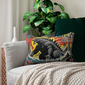 Peut inclure: Un coussin décoratif avec un motif d'affiche de film japonais vintage représentant un monstre ressemblant à Godzilla dans un décor urbain. L'affiche est en japonais et comporte le texte "ゴジラ" et "怪獣大戦争".