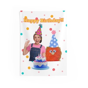 May include: A white background with colourful polka dots. A girl wearing a pink shirt and blue overalls is holding a party hat. A fuzzy orange monster with a blue and white party hat is standing next to her. A blue and white cake with pink frosting and candles is in front of them. The text "Happy Birthday!" is at the top of the image.