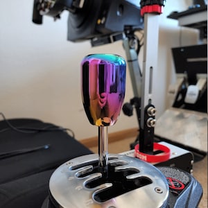 May include: A close-up of a chrome gear stick knob with a rainbow iridescent finish. The knob is attached to a black gear stick base with a silver gear pattern.