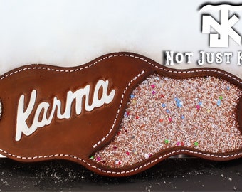 May include: Brown leather belt with a sparkly, glittery center section. The belt has a silver buckle with a cactus design and the word "Karma" is embossed on the leather.