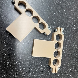 May include: Two beige plastic pipe clamps with multiple holes for pipes. The clamps have metal screws for attaching to a surface.