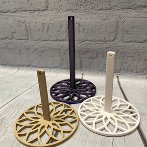 May include: Three decorative stands with a mandala design. The stands are made of plastic and come in white, beige, and purple.