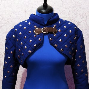 May include: A blue quilted cropped jacket with silver studs and a brown leather strap closure.