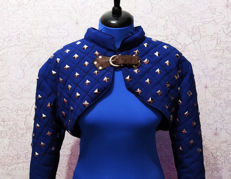 May include: A blue quilted cropped jacket with silver studs and a brown leather strap closure.