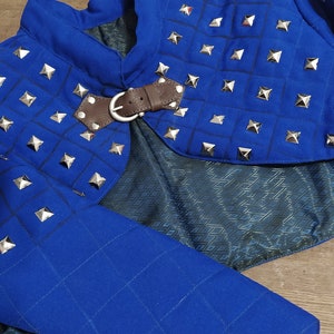 May include: Blue quilted fabric shoulder armor with silver pyramid-shaped studs and a brown leather strap with a buckle.