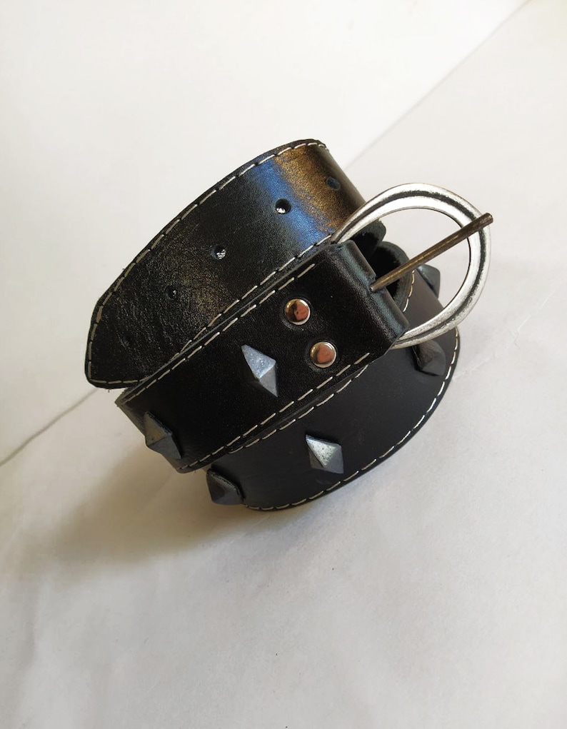 Puede incluir: Un cintur&oacute;n de cuero negro con tachuelas de pir&aacute;mide plateadas y una hebilla plateada. El cintur&oacute;n tiene costuras blancas.