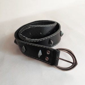 Puede incluir: Un cintur&oacute;n de cuero negro con tachuelas plateadas y una hebilla plateada. El cintur&oacute;n tiene costuras blancas alrededor de los bordes.