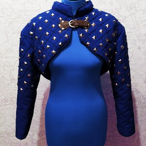 May include: A blue quilted cropped jacket with silver studs and a brown leather buckle closure.