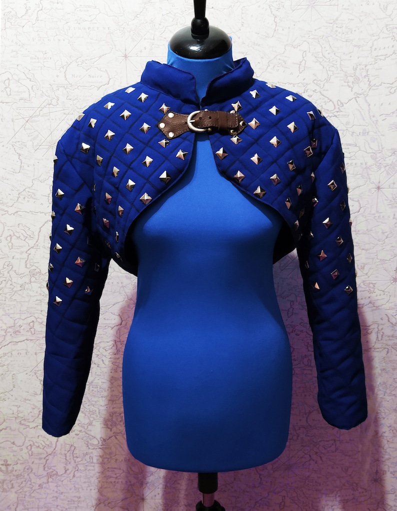 May include: A blue quilted cropped jacket with silver studs and a brown leather buckle closure.