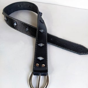 Puede incluir: Un cintur&oacute;n de cuero negro con tachuelas de forma piramidal plateadas y una hebilla ovalada plateada.