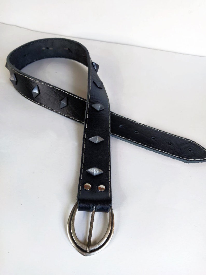 Puede incluir: Un cintur&oacute;n de cuero negro con tachuelas de forma piramidal plateadas y una hebilla ovalada plateada.