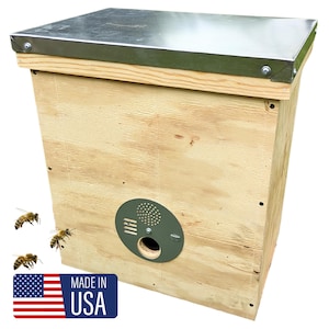 May include: A wooden beehive with a metal top and a circular entrance. The hive is made of light-colored wood and has a dark green circular entrance. The words "MADE IN USA" are printed on a blue rectangle with the American flag.