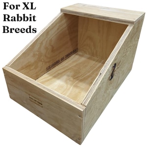 May include: A wooden rabbit hutch with a slanted roof and a handle. The text "For XL Rabbit Breeds" is visible on the top left. The hutch is made of light-colored plywood.