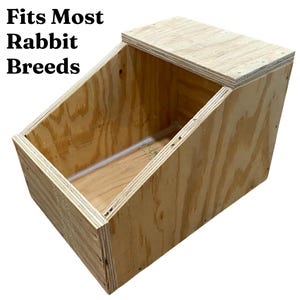 May include: A wooden rabbit nesting box with a hinged lid. The box is made of plywood and has a sloped front. The text "Fits Most Rabbit Breeds" is printed on the front of the box.
