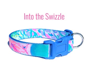 May include: A blue and pink patterned dog collar with a blue plastic buckle and a silver metal ring. The collar has the text "Into the Swizzle" printed on it.