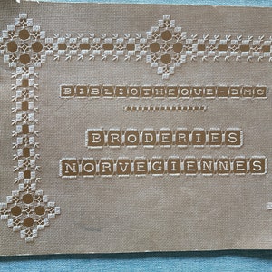 May include: A beige card with a white embroidered border. The card has the text "Bibliotheque DMC" and "Broderies Norvegiennes" in brown.