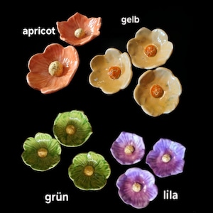 May include: A collection of ten small ceramic flower-shaped dishes in various colors including apricot, yellow, green, and purple. Each dish features a textured center and smooth, curved petals. The text labels apricot, gelb, gr&uuml;n, and lila are visible.