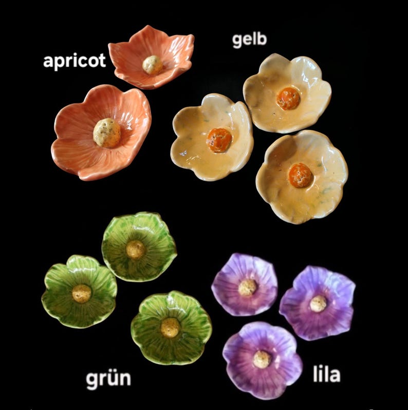 May include: A collection of ten small ceramic flower-shaped dishes in various colors including apricot, yellow, green, and purple. Each dish features a textured center and smooth, curved petals. The text labels apricot, gelb, gr&uuml;n, and lila are visible.