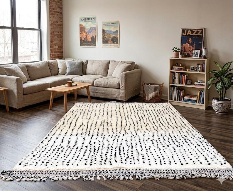 May include: A large, rectangular rug with a white background and a pattern of black vertical dashes. The rug has a fringe border and is placed in a living room with a beige sectional sofa, wooden coffee table, and a bookshelf.