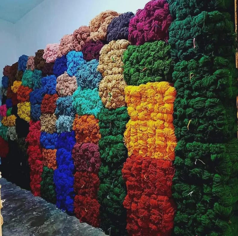 May include: A wall of colorful yarn bundles in shades of pink, blue, green, yellow, and orange. The yarn is stacked in neat rows, creating a visually appealing display of textures and hues. Ideal for crafting projects.