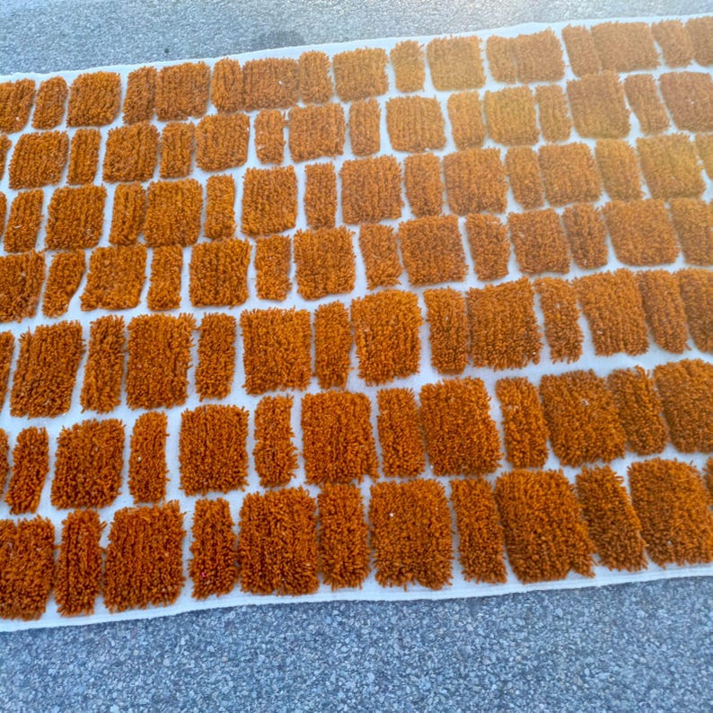 May include: A rectangular rug with a repeating pattern of orange, textured, rectangular shapes against a white background. The rug's design resembles a brick wall, with each shape having a slightly raised, plush appearance.