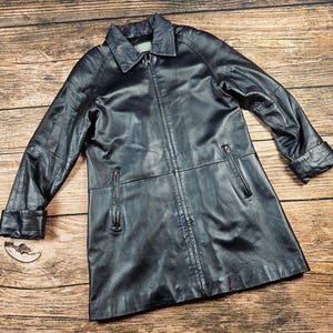 May include: A long black leather jacket with a zipper closure and pockets. The jacket has a collar and a slightly fitted silhouette.