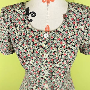 May include: A short-sleeved dress with a button-up front and a floral print featuring small pink, white, and blue flowers on a black background.